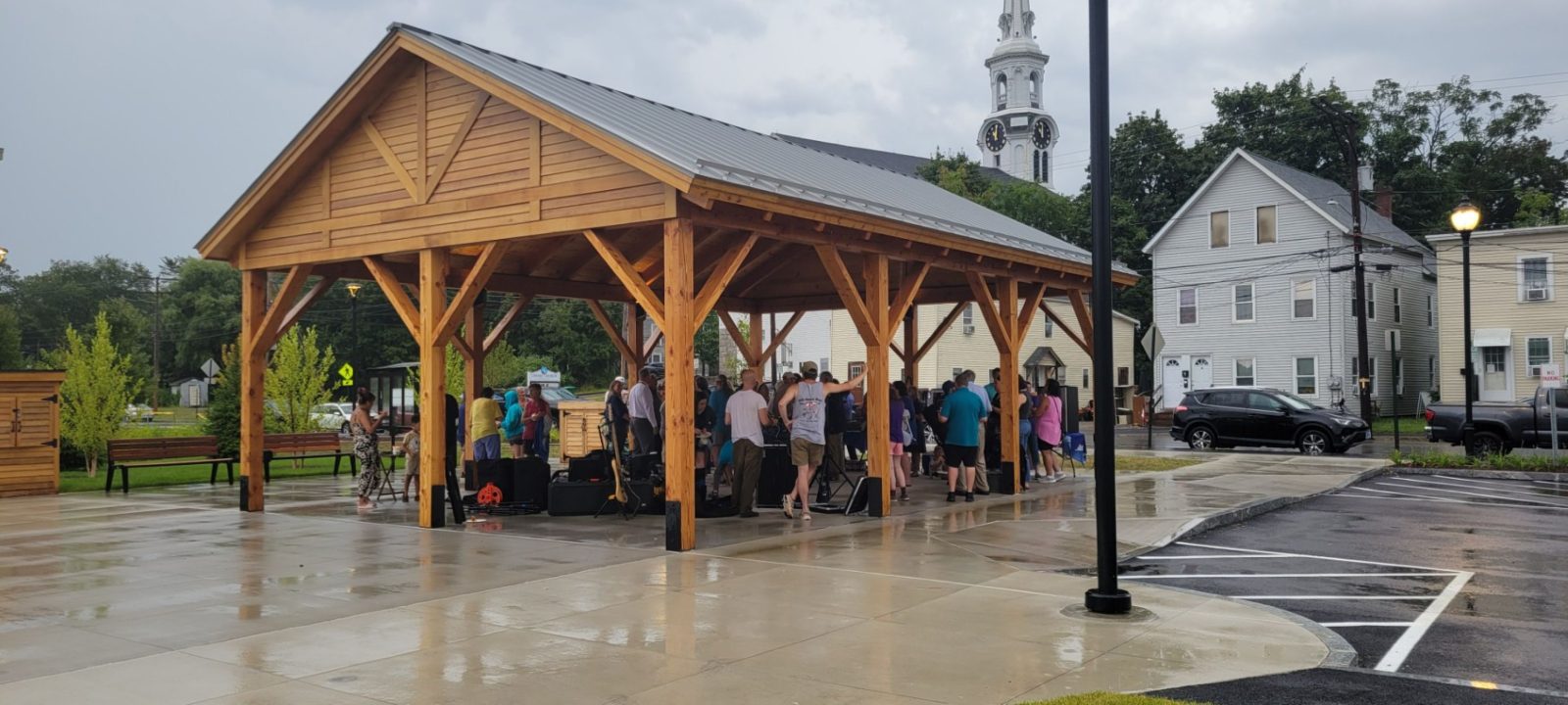 A group of people gathers outside a wooden pavilion, engaging in conversation under its shelter.